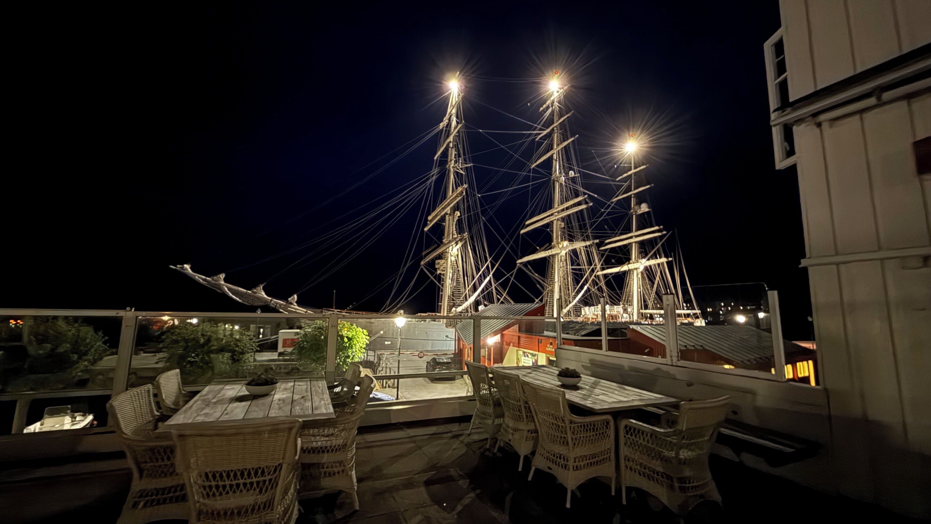 Une terrasse sur le toit, avec des tables et des chaises, une grande maquette de navire et un bâtiment à la façade blanche.