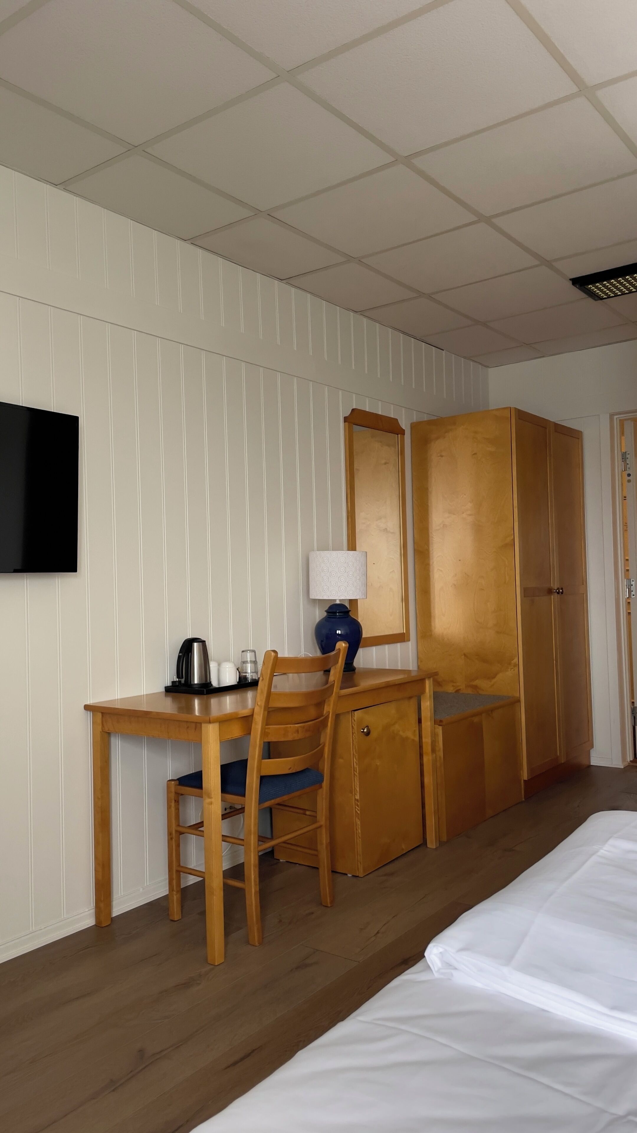 Ein Hotelzimmer mit einem Holztisch, einem Sessel, einem Bett, einem Fernseher und einem Kleiderschrank.