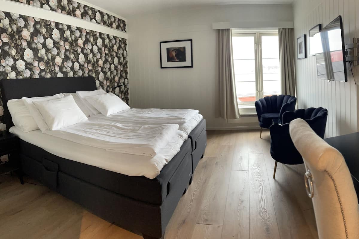 Habitación de hotel con una cama grande, un escritorio con silla, un televisor y una ventana con cortinas.
