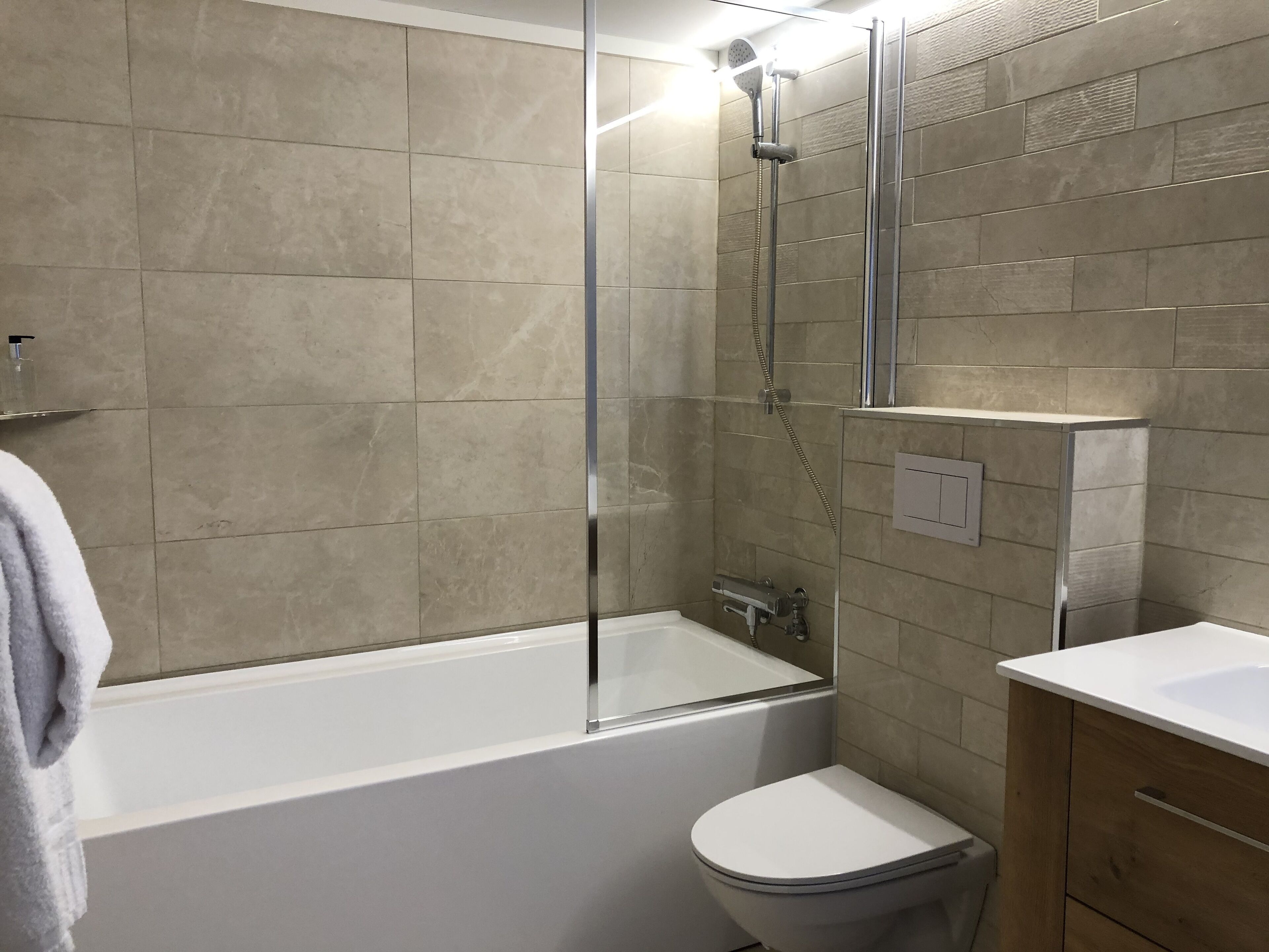 Un baño moderno con ducha de vidrio, una bañera blanca y un mueble de madera.