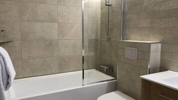 Un baño moderno con ducha de vidrio, una bañera blanca y un mueble de madera.