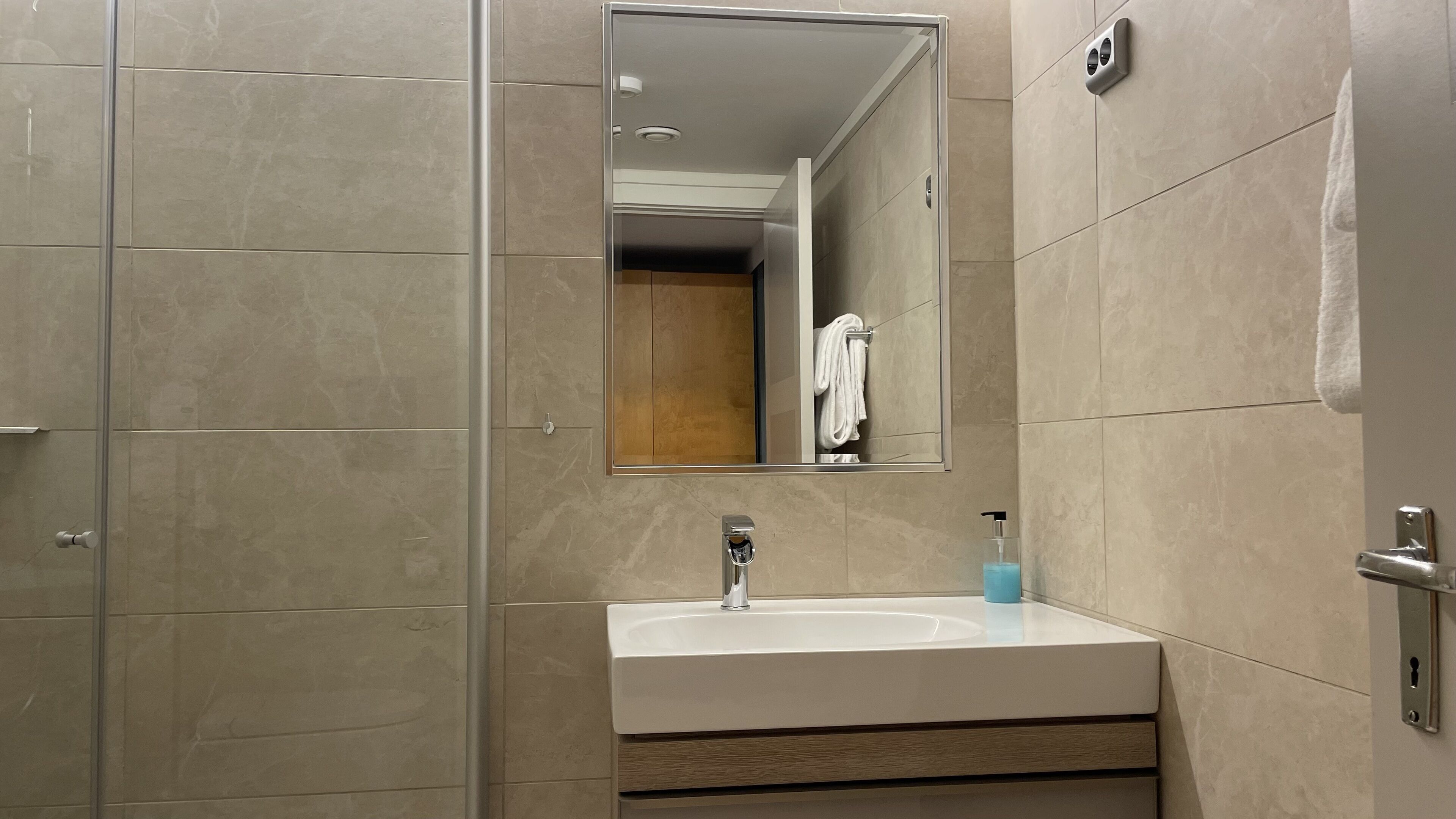 Un baño con un lavamanos blanco, un espejo y una toalla colgada en la pared.