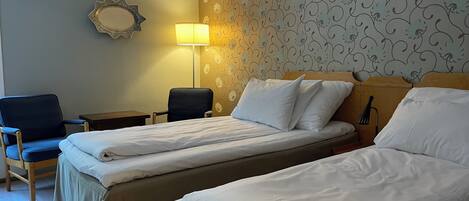 Quarto de hotel com duas camas, uma mesa, uma cadeira, uma luminária e um espelho decorativo.
