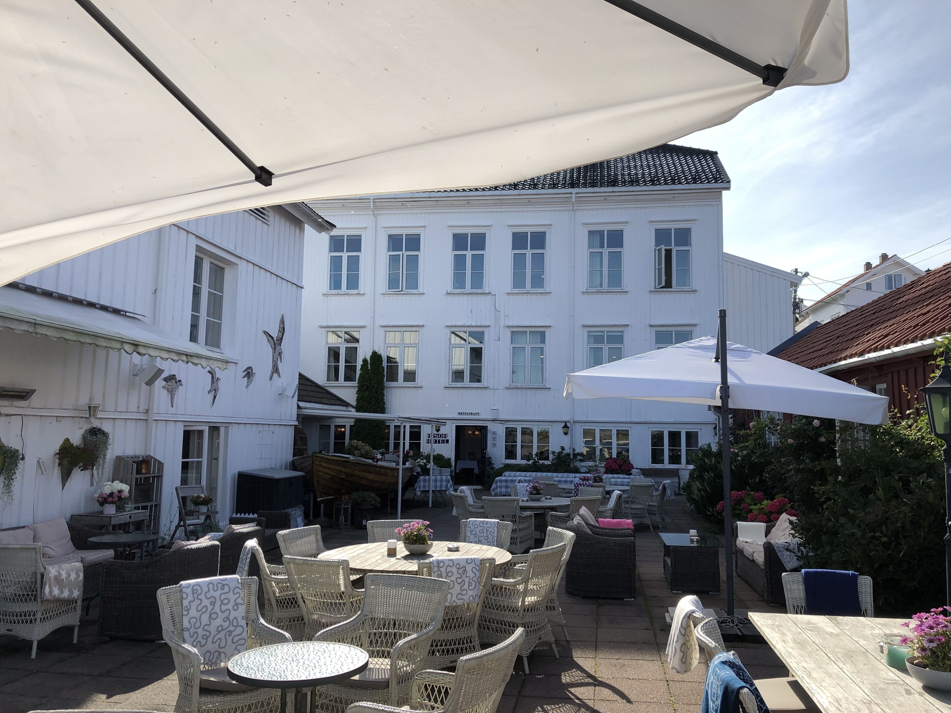 An outdoor seating area with wicker furniture and umbrellas, a white building with multiple windows in the background, and a sign that reads "RESTAURANT".