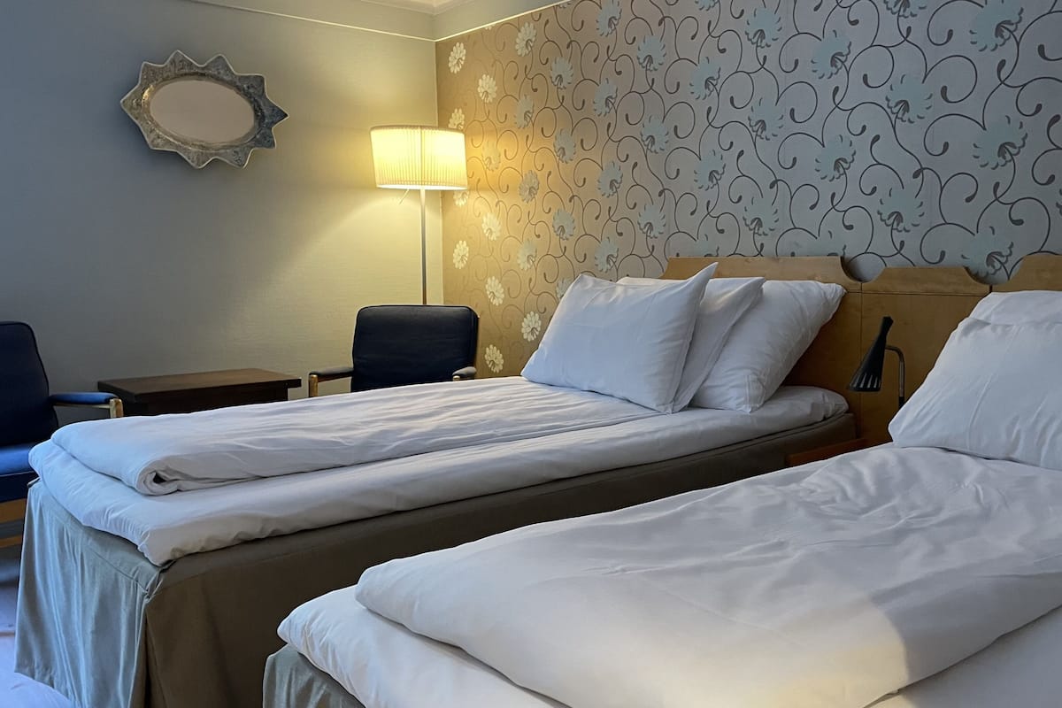 Habitación de hotel con dos camas, un escritorio, una silla, una lámpara y un espejo decorativo en la pared.