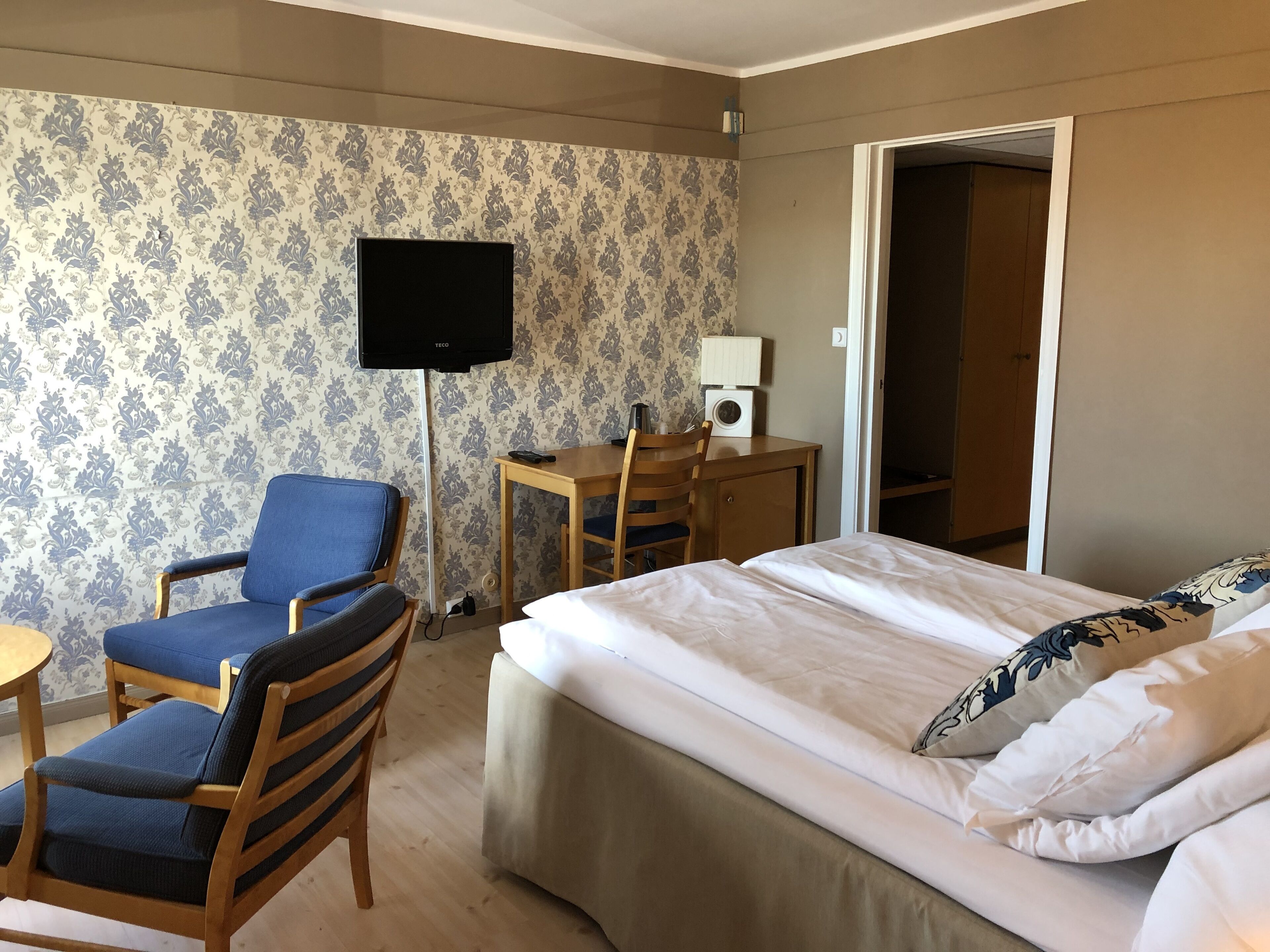 A hotel room with a bed, a desk with a chair, a television, and a wardrobe.