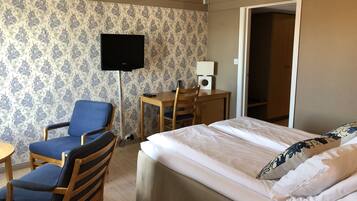 A hotel room with a bed, a desk with a chair, a television, and a wardrobe.