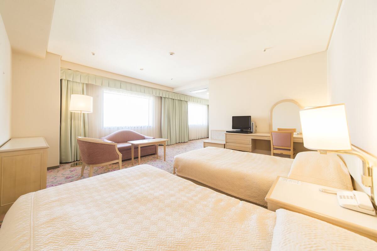 Une chambre d’hôtel avec deux lits, un bureau, une chaise, une télévision et une lampe.