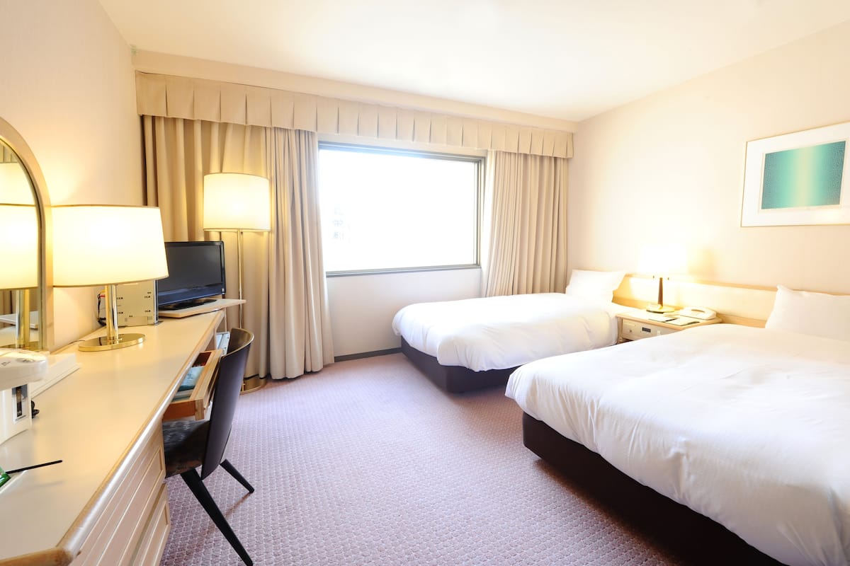 Une chambre d’hôtel avec deux lits, un bureau avec un ordinateur, une télévision et une fenêtre avec des rideaux.