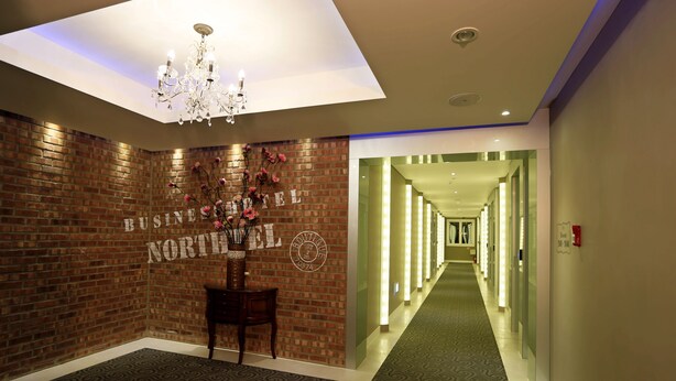Un vestíbulo de hotel con pared de ladrillo, un candelabro, un mostrador de recepción y un largo pasillo con letreros iluminados.