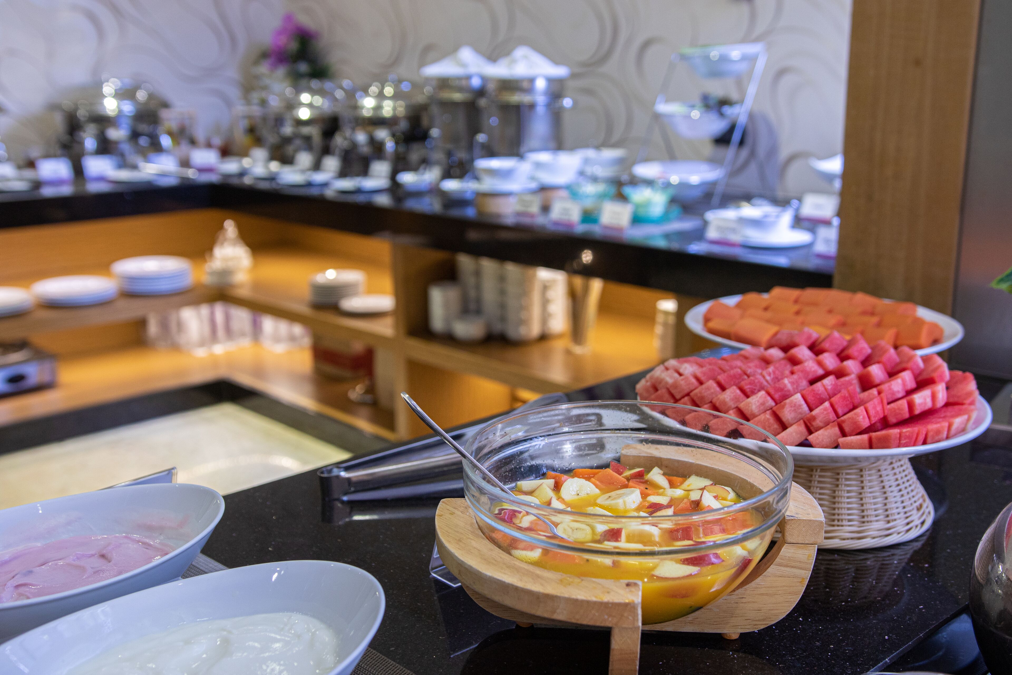 Un buffet proposant divers plats, notamment des fruits, un saladier de fruits variés et une assiette de pastèque.