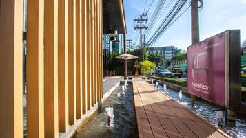 A wooden deck with a water feature, a sign for Hotel Icon, and a view of the street with cars and buildings.
