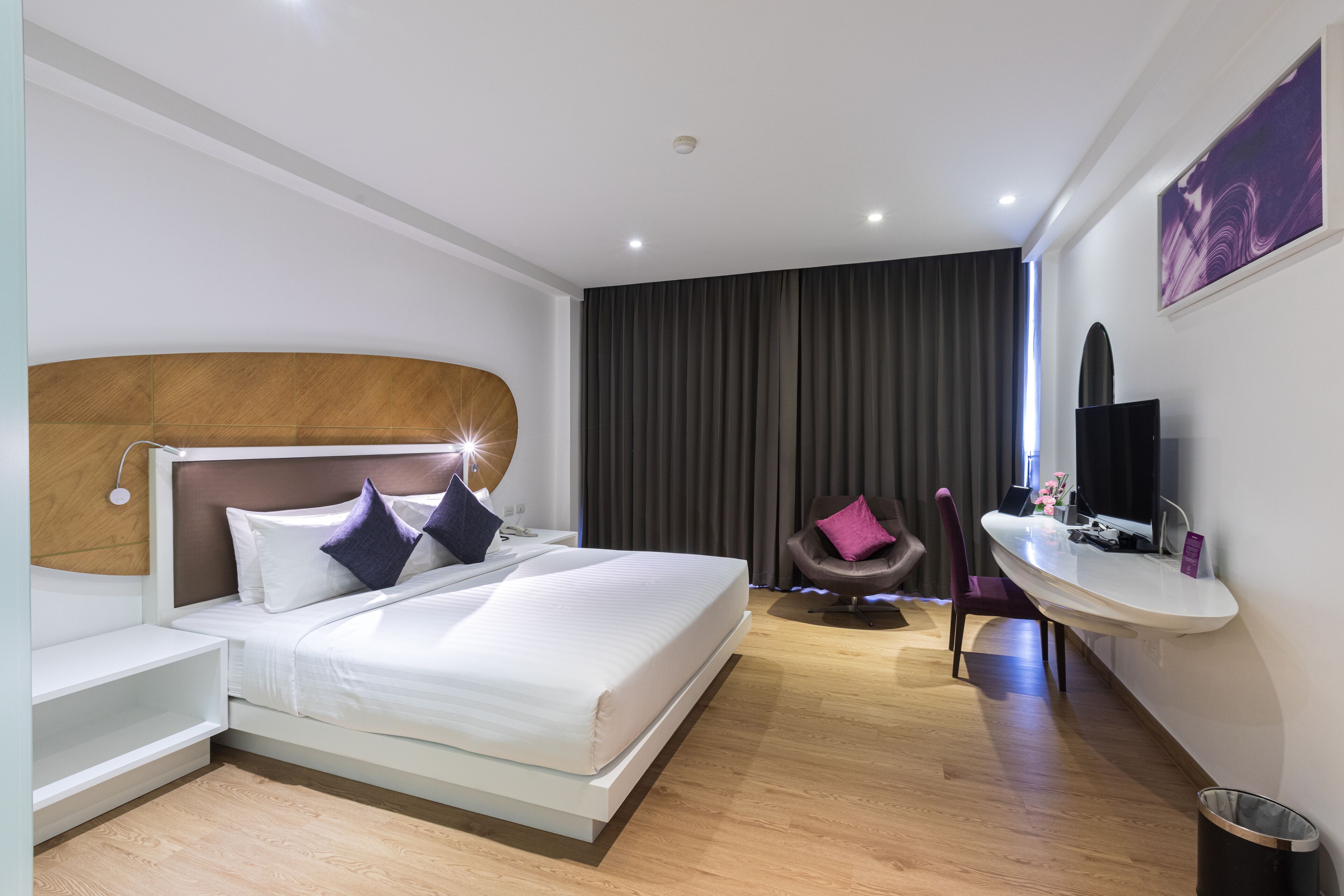 Une chambre d’hôtel moderne avec un grand lit, une table de chevet, une coiffeuse avec un miroir et une chaise.