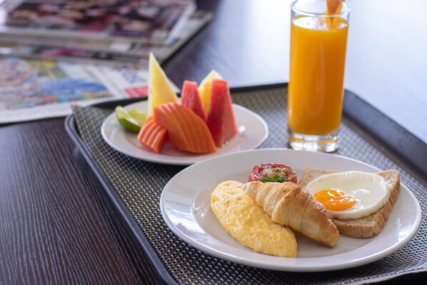 A breakfast tray with croissants, a fried egg, and fruit on a table.