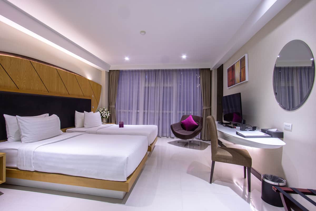 Een moderne hotelkamer met twee bedden, een bureau, een stoel, een computer en een groot raam met gordijnen.