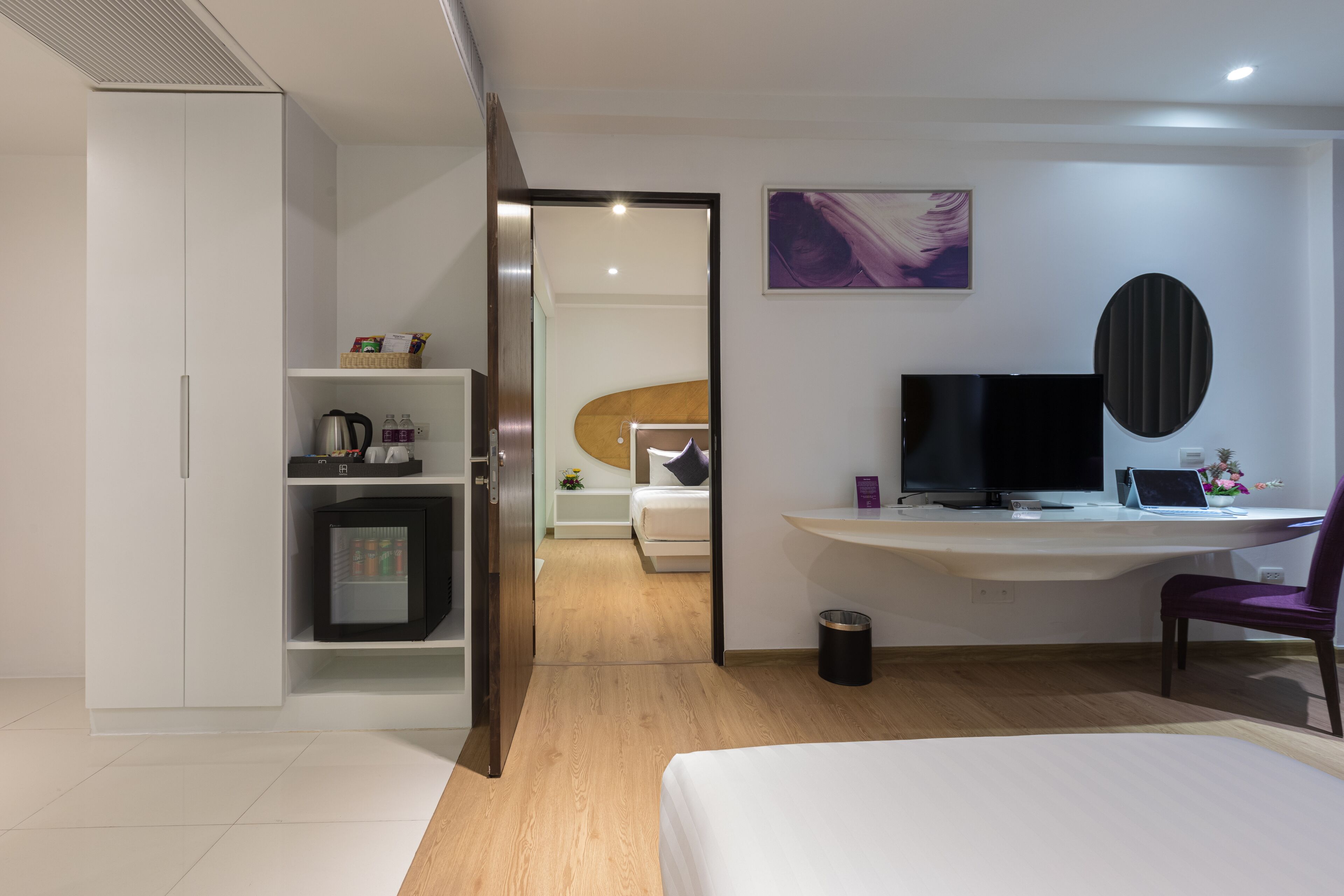 Una habitación de hotel moderna con una cama, un escritorio con una computadora, un televisor y un armario.