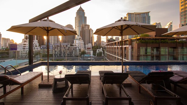 Uma área de piscina no terraço com espreguiçadeiras e guarda-sóis, com vista para um horizonte urbano repleto de edifícios modernos.