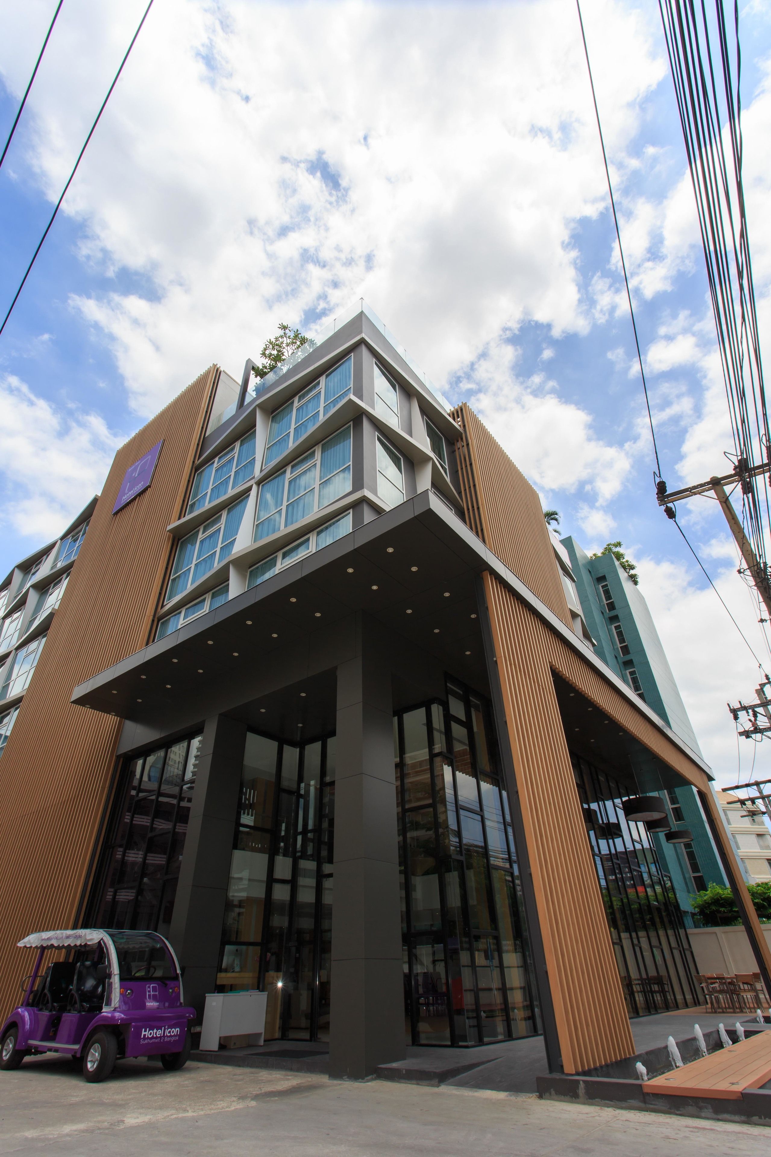 A modern hotel with a prominent entrance, large windows, and a small purple vehicle in front.