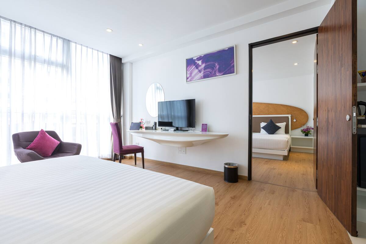 Een hotelkamer met een bed, een bureau met een computer, een televisie en uitzicht op een andere kamer.