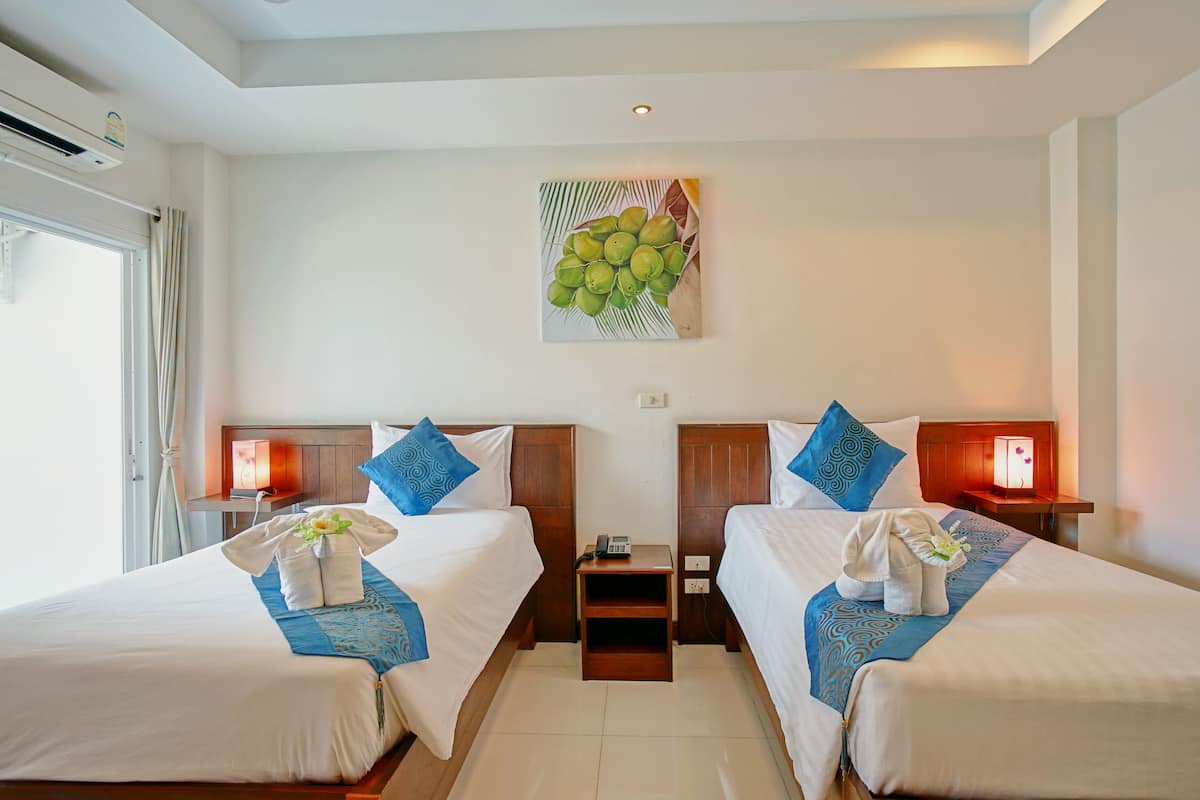 A hotel room with two beds, a nightstand with a phone, and a wall-mounted artwork of coconuts.