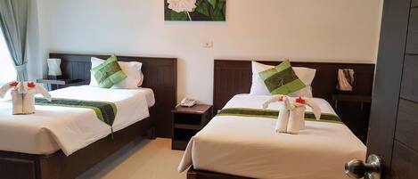 Two neatly made beds with white linens, green and patterned pillows, and towels arranged as a decorative element.