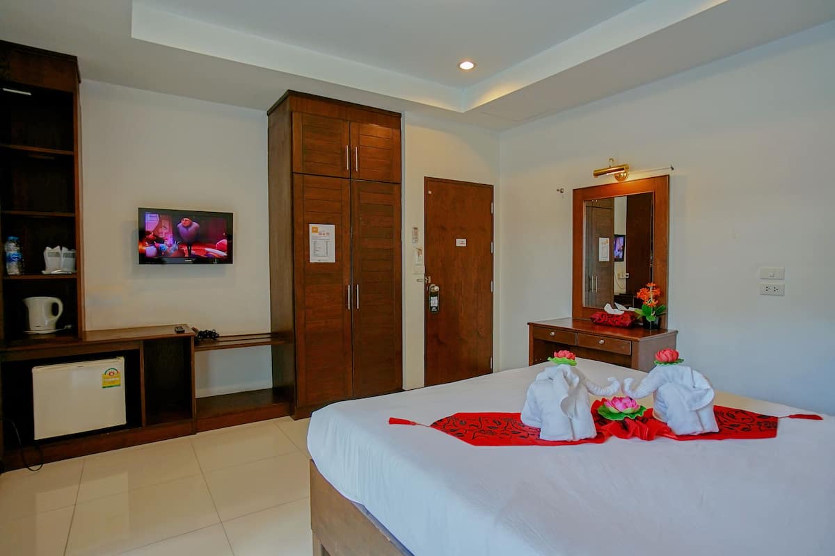 A hotel room with a bed, a television, a wardrobe, a desk, and a small refrigerator.