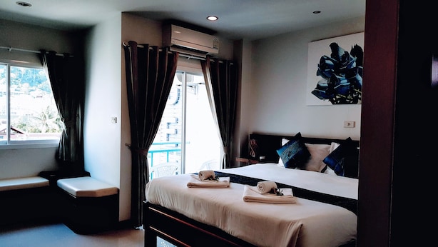 Een hotelkamer met een bed, een bankje, een raam met gordijnen en een wandairconditioner.