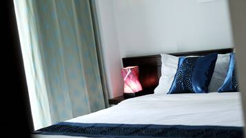 Habitación de hotel con una cama bien hecha, una mesita de noche con lámpara y una ventana con cortinas.