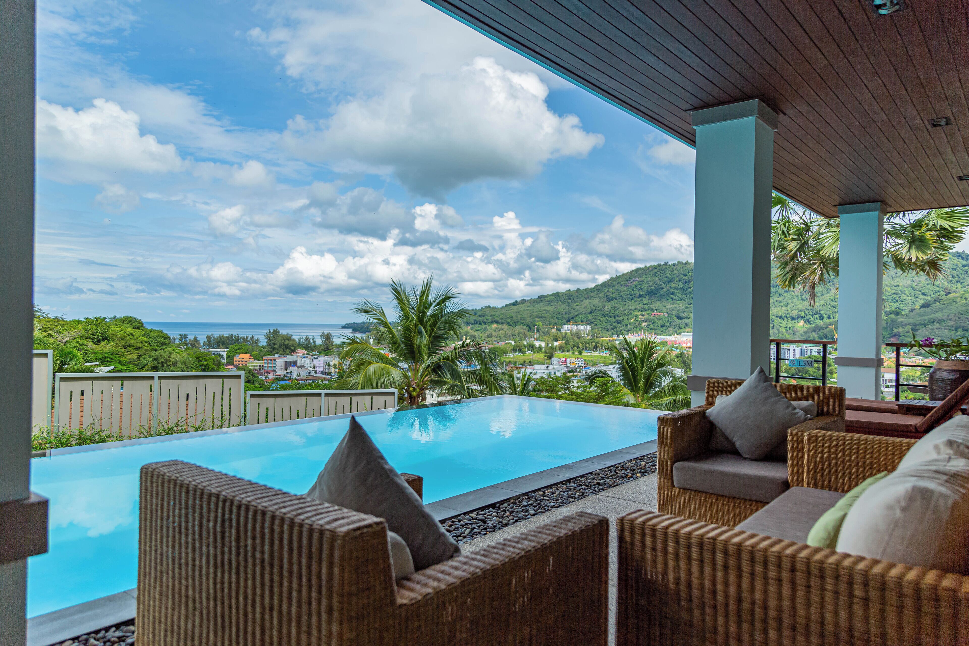 A pool area with wicker furniture and a view of the sea and hills.