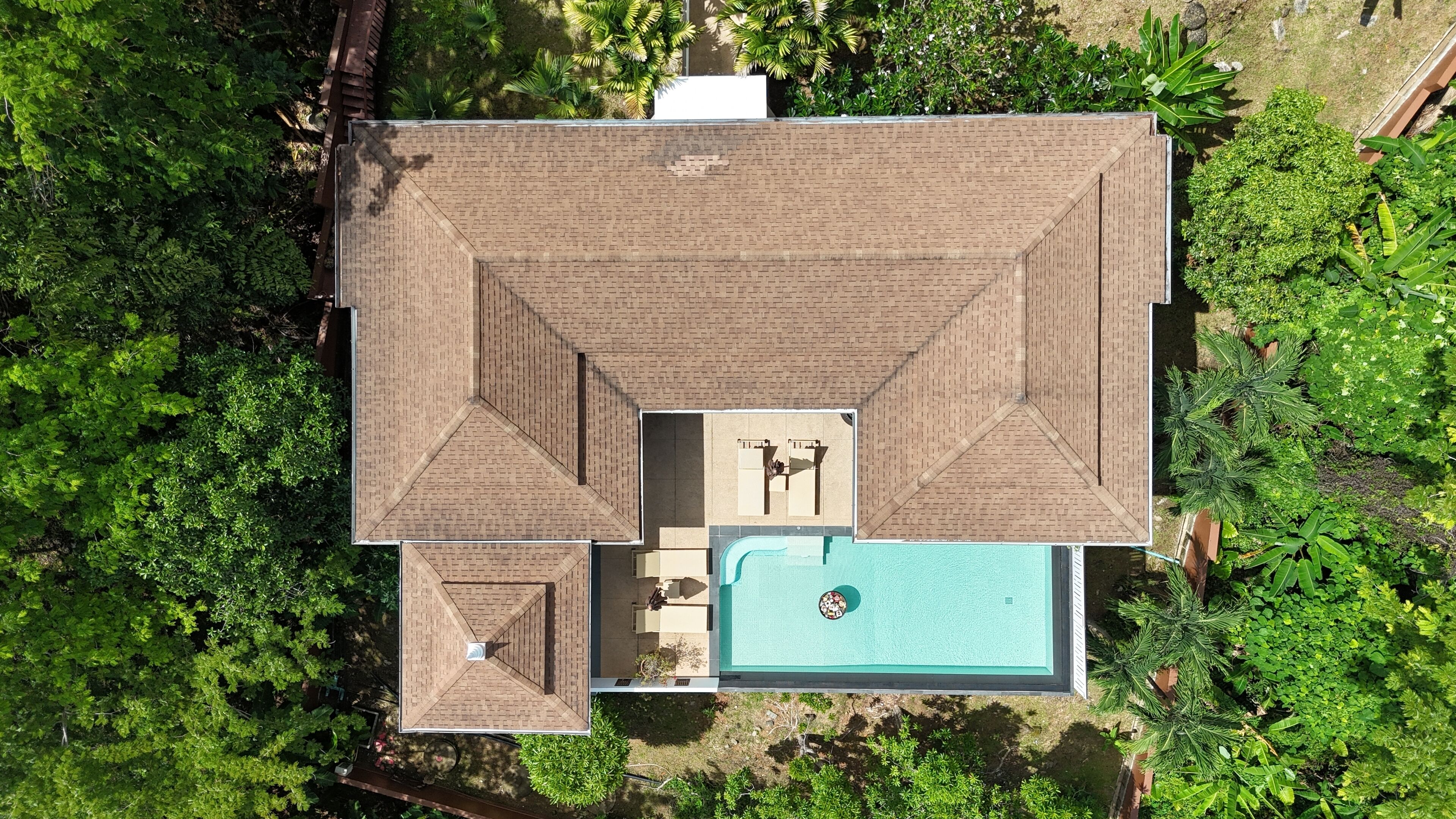 An aerial view of a house with a swimming pool, surrounded by dense greenery.