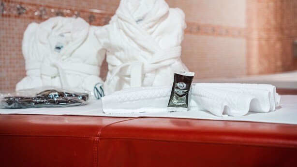 A bathroom with two white towels, a pair of slippers, and a small bottle on a red surface.