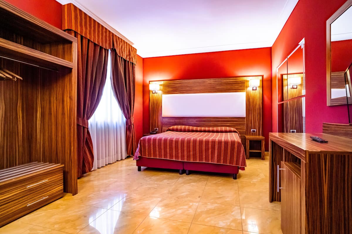 Une chambre d’hôtel avec un grand lit, des meubles en bois et un mur d’accent de couleur rouge.