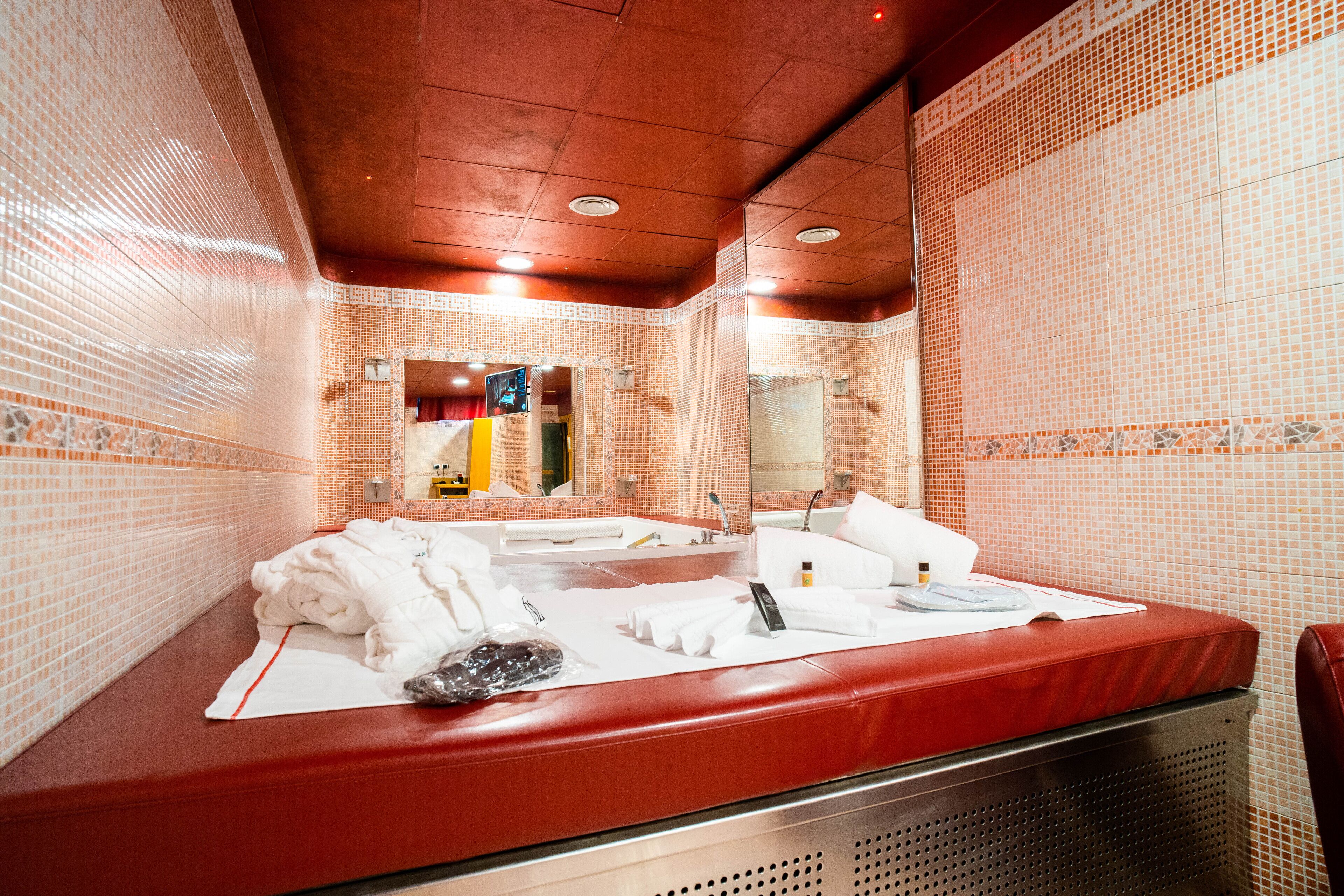 Une salle de bain avec une baignoire rouge, des serviettes blanches et un miroir.