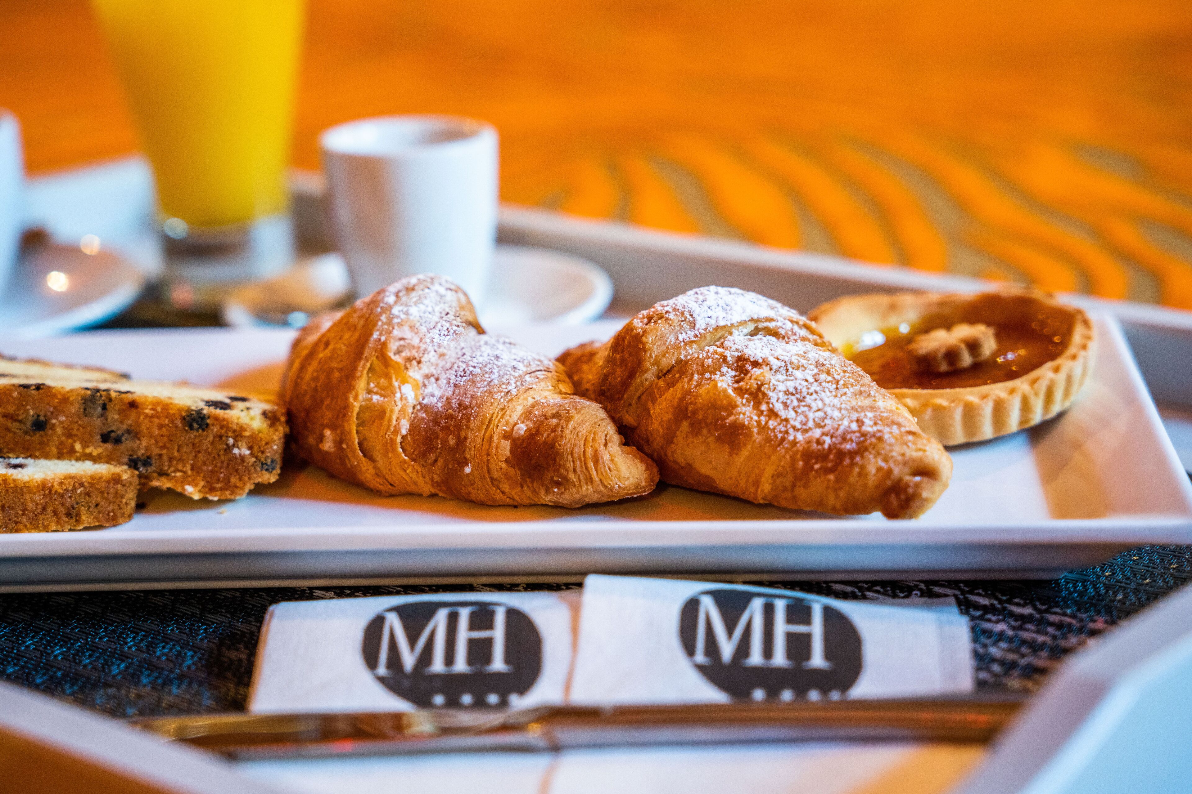 A breakfast tray with croissants, a muffin, and a tart, along with a cup of coffee and a glass of orange juice.