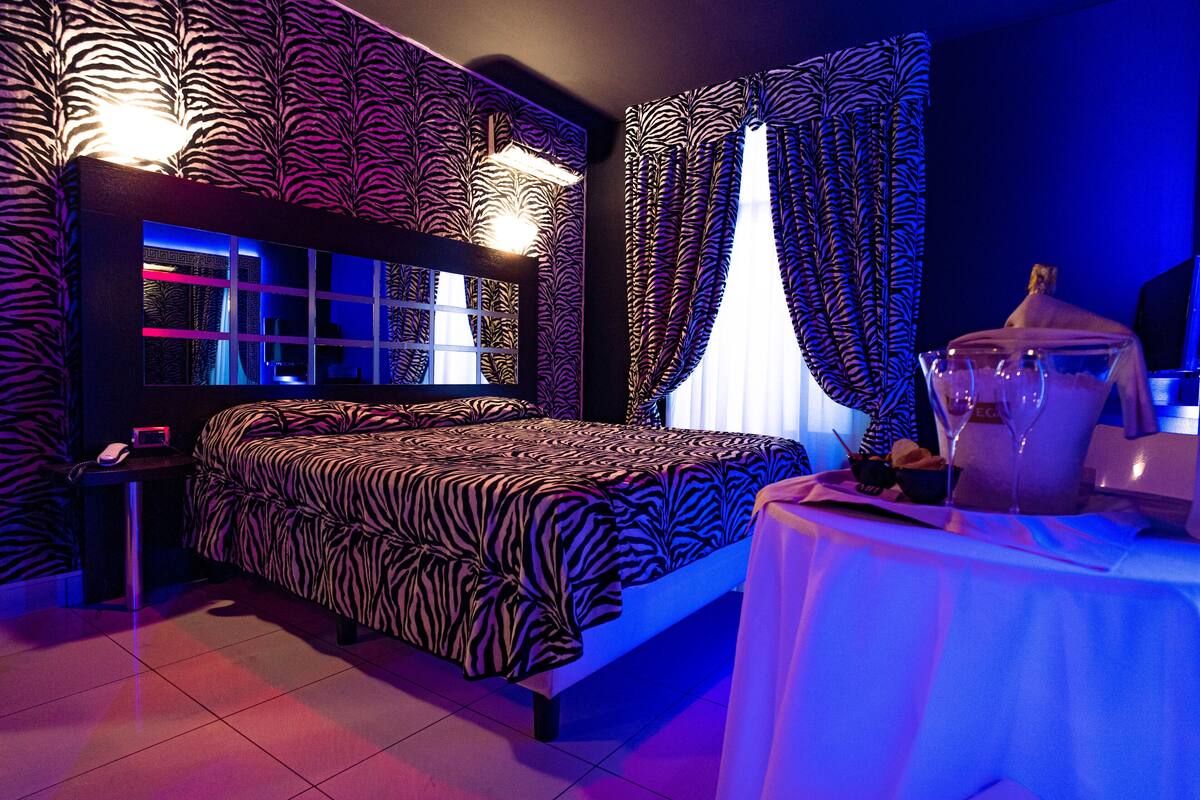 Une chambre à coucher avec une couvre-lit à motifs zébrés, une table de chevet avec une lampe et une fenêtre ornée de rideaux à motifs zébrés.