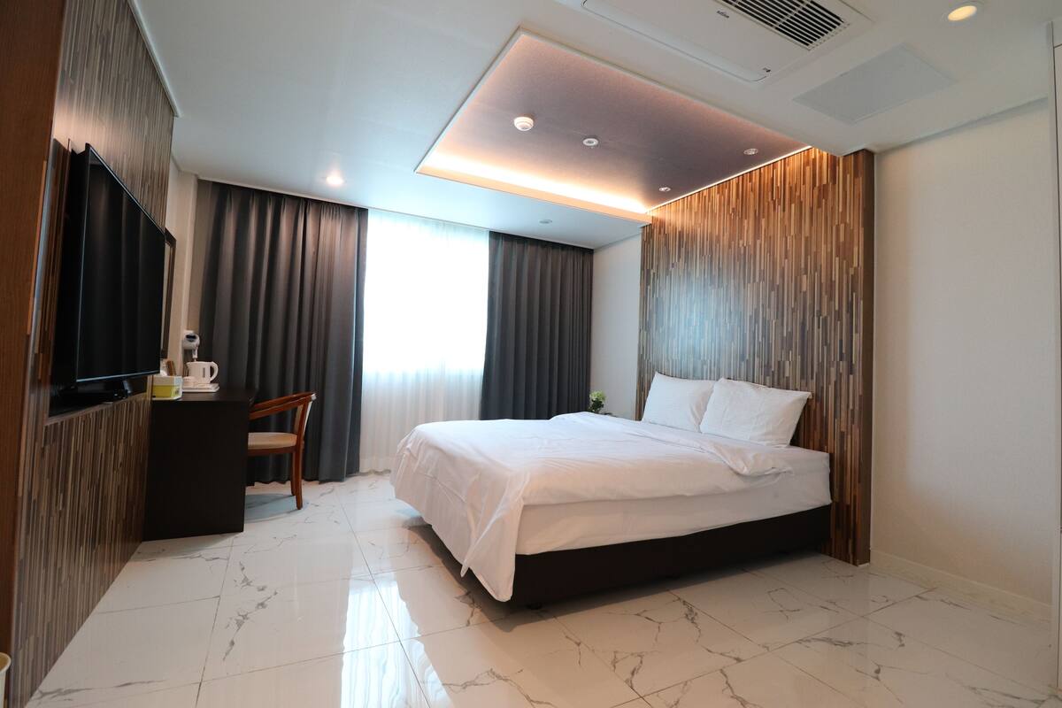 Una habitación de hotel moderna con una cama grande, un escritorio con una silla y un televisor.
