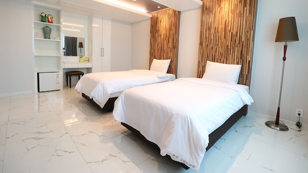 Habitación de hotel con dos camas, un armario, una tocador con espejo y una lámpara de pie.