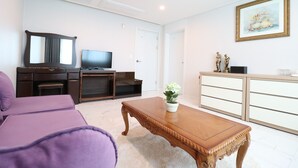 Una sala de estar con un sofá, una mesa de centro de madera, un televisor, un mueble y un cuadro en la pared.