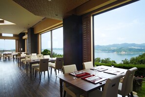 Un restaurante con una larga mesa dispuesta para comer, ventanas amplias que ofrecen vistas al mar y a las montañas.