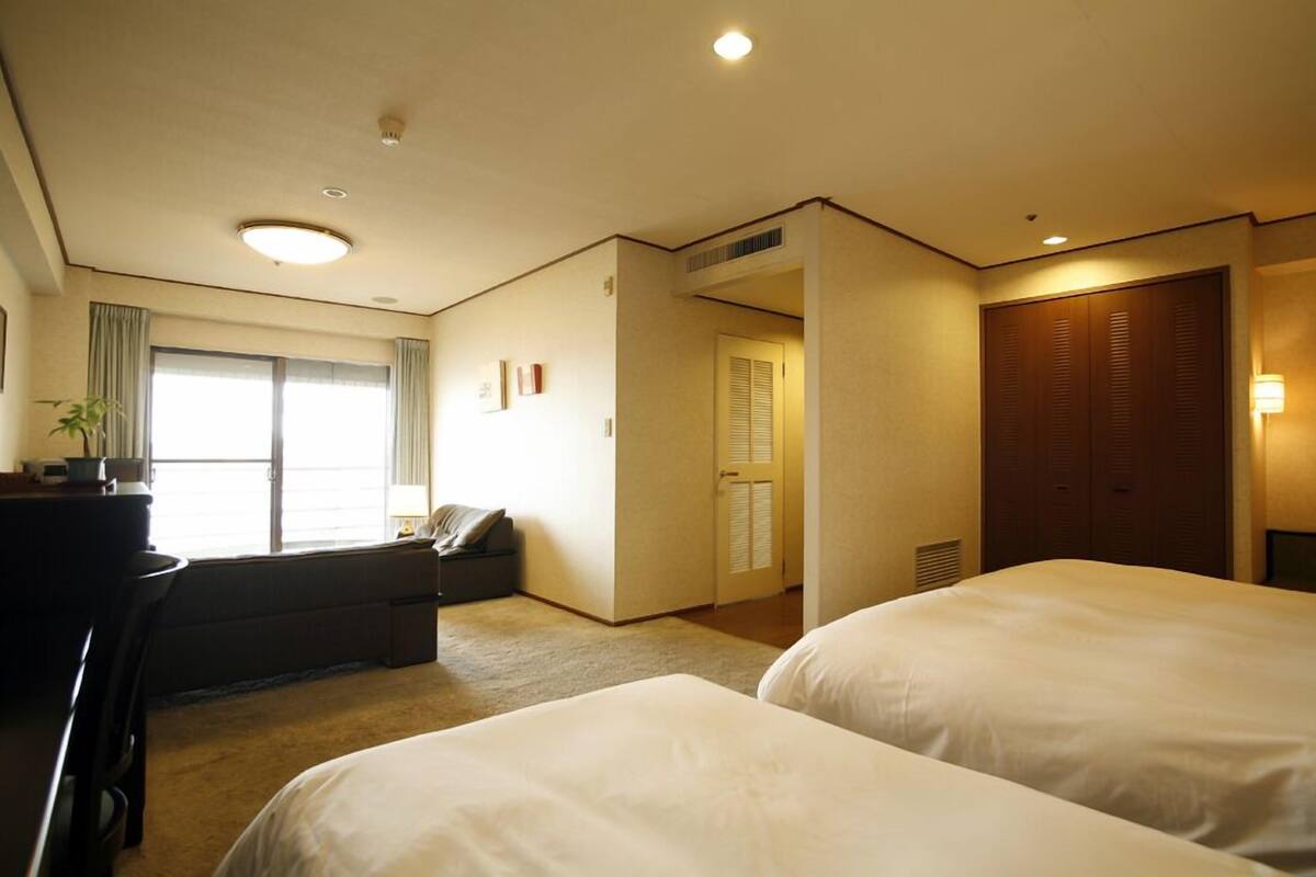 Een hotelkamer met twee bedden, een bureau, een stoel, een bank en een raam met gordijnen.