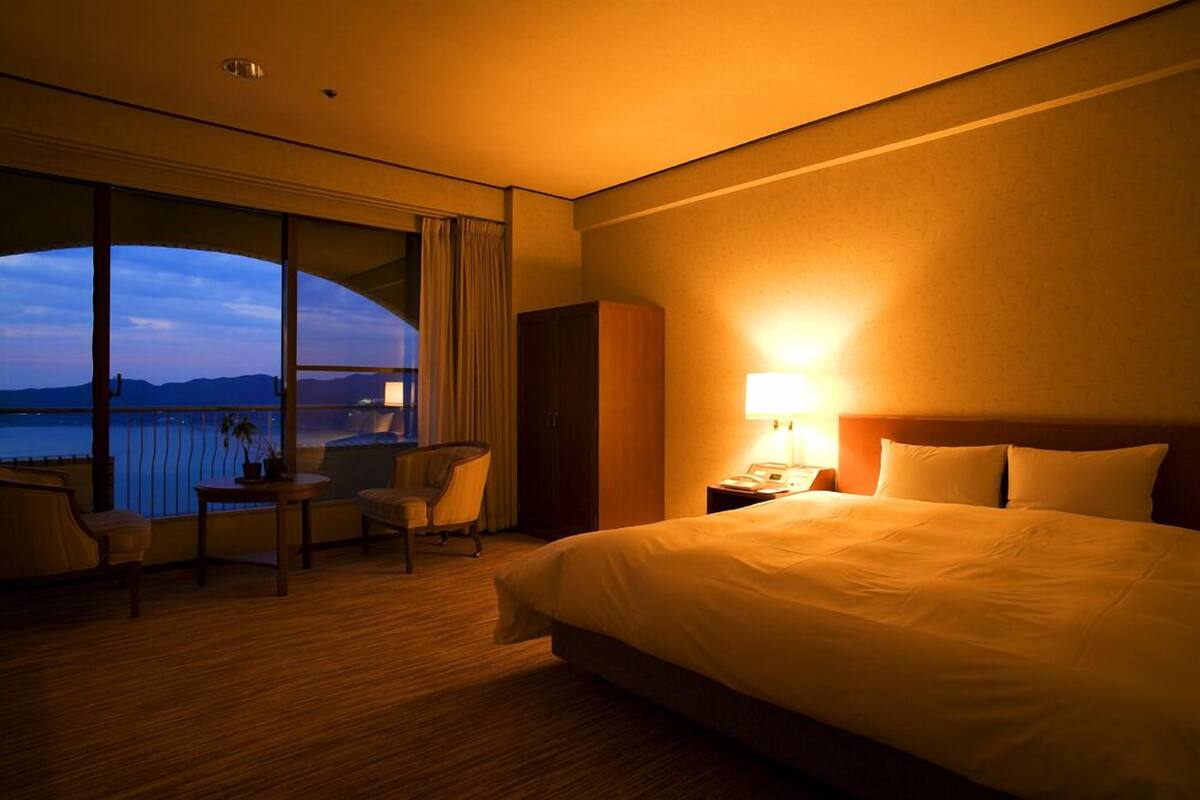 Een hotelkamer met een groot bed, een bureau met stoel, een nachtkastje en uitzicht op het water.