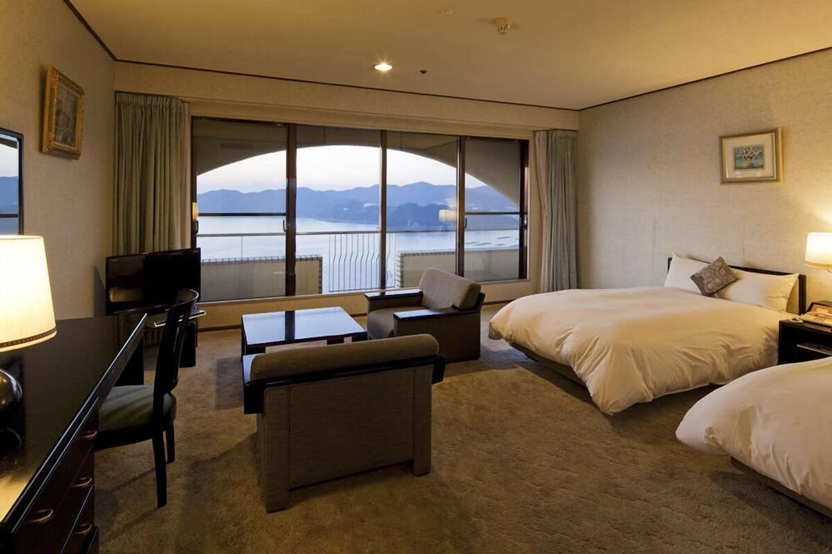 Een hotelkamer met een groot raam, een bed, een bureau, een stoel en een televisie.