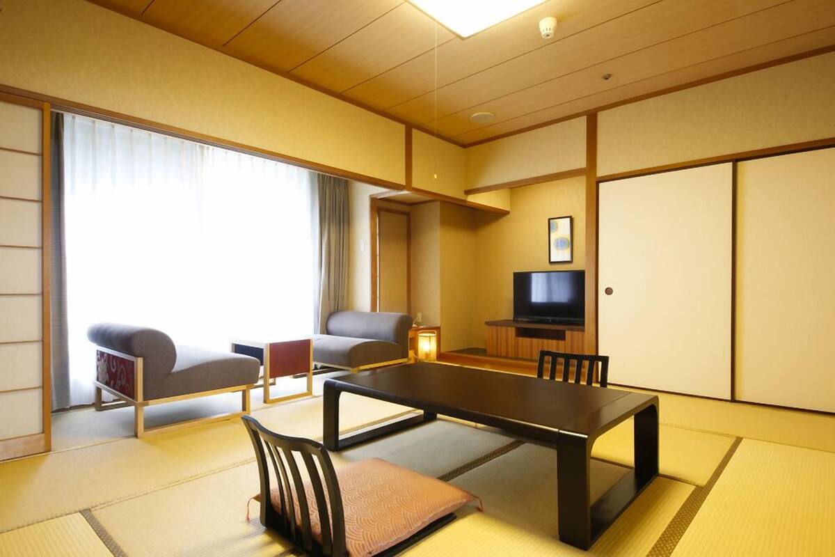 Een traditionele Japanse kamer met tatami vloerbedekking, een lage tafel, twee banken, een televisie en schuifdeuren.