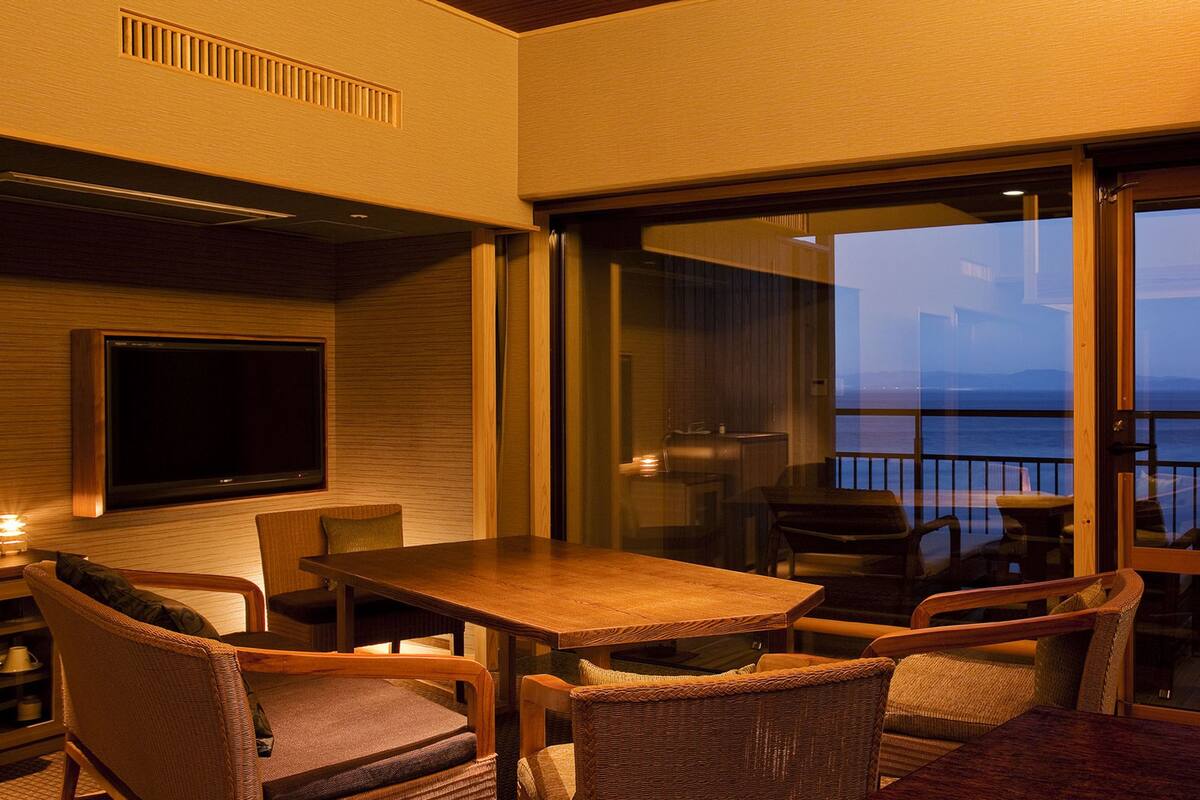 A balcony with a wooden table and wicker chairs, overlooking a body of water.