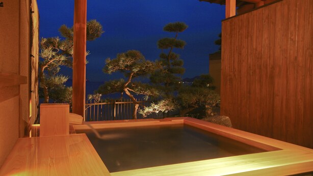A wooden hot spring bath with a view of pine trees and a wooden fence. - Hotel New Awaji (Sumoto)