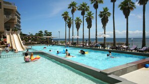 A swimming pool with palm trees, lounge chairs, and a slide. - Hotel New Awaji (Sumoto)