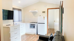 A compact kitchen with white cabinets, a microwave, a gas stove, and a refrigerator. There's a black sofa with cushions in the living area. - Riverview Tourist Park (Margaret River)