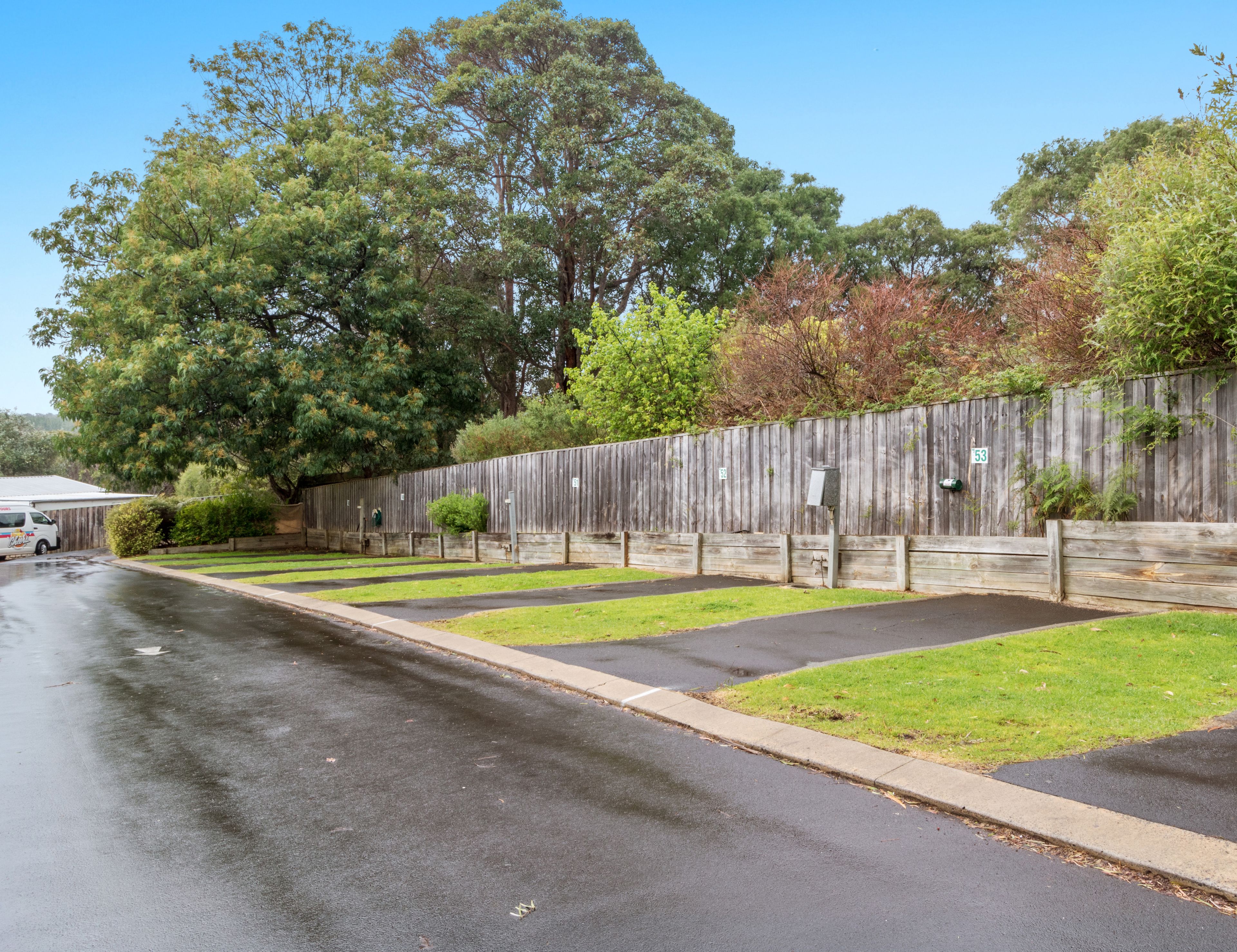 A parking lot with a wooden fence, a grassy area, and a building in the background.