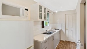 A modern kitchen with white cabinets, a microwave, a sink, and a window with a view. - Riverview Tourist Park (Margaret River)