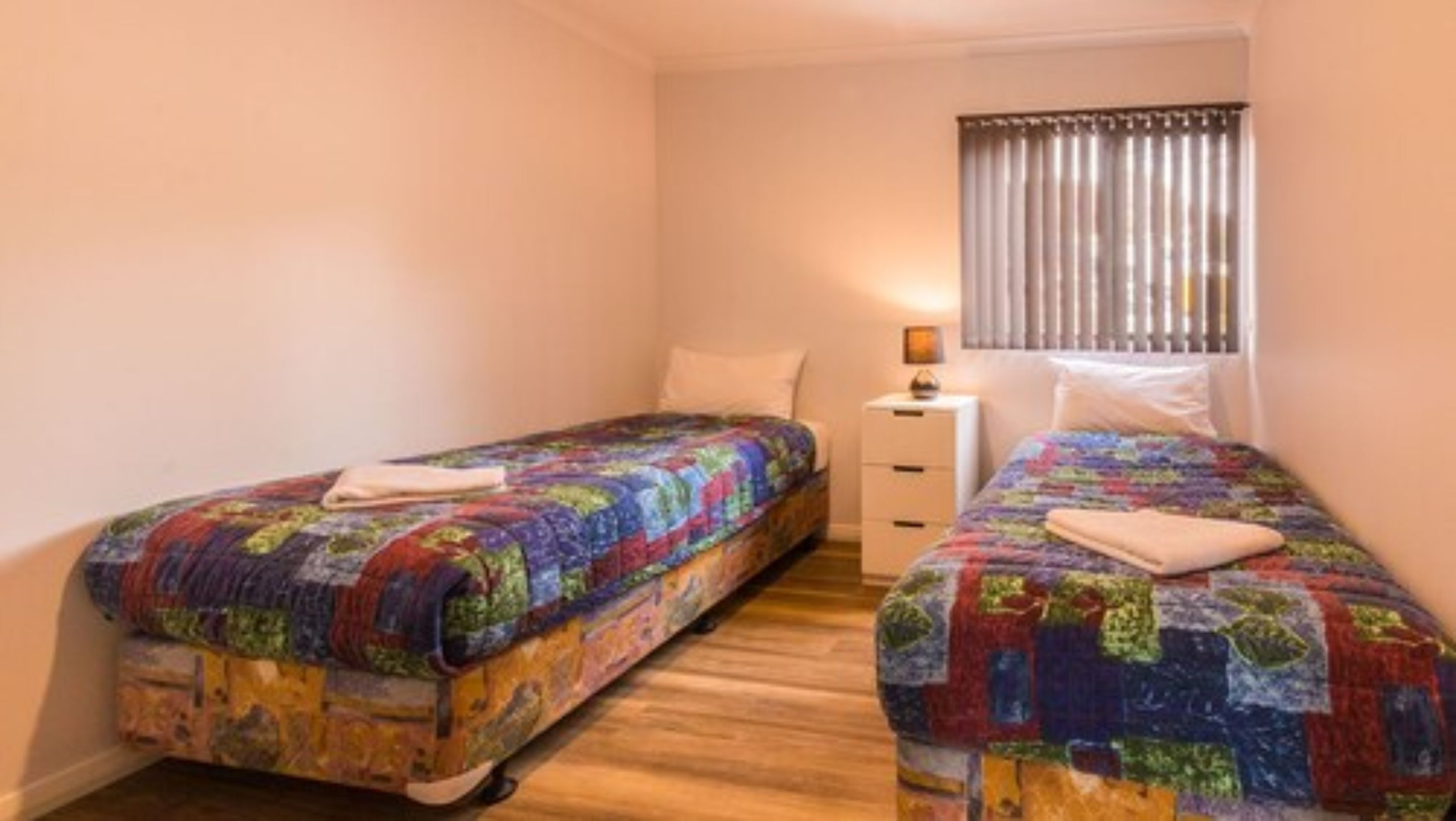 A small, cozy bedroom with two single beds, each with colorful quilts and neatly folded towels.